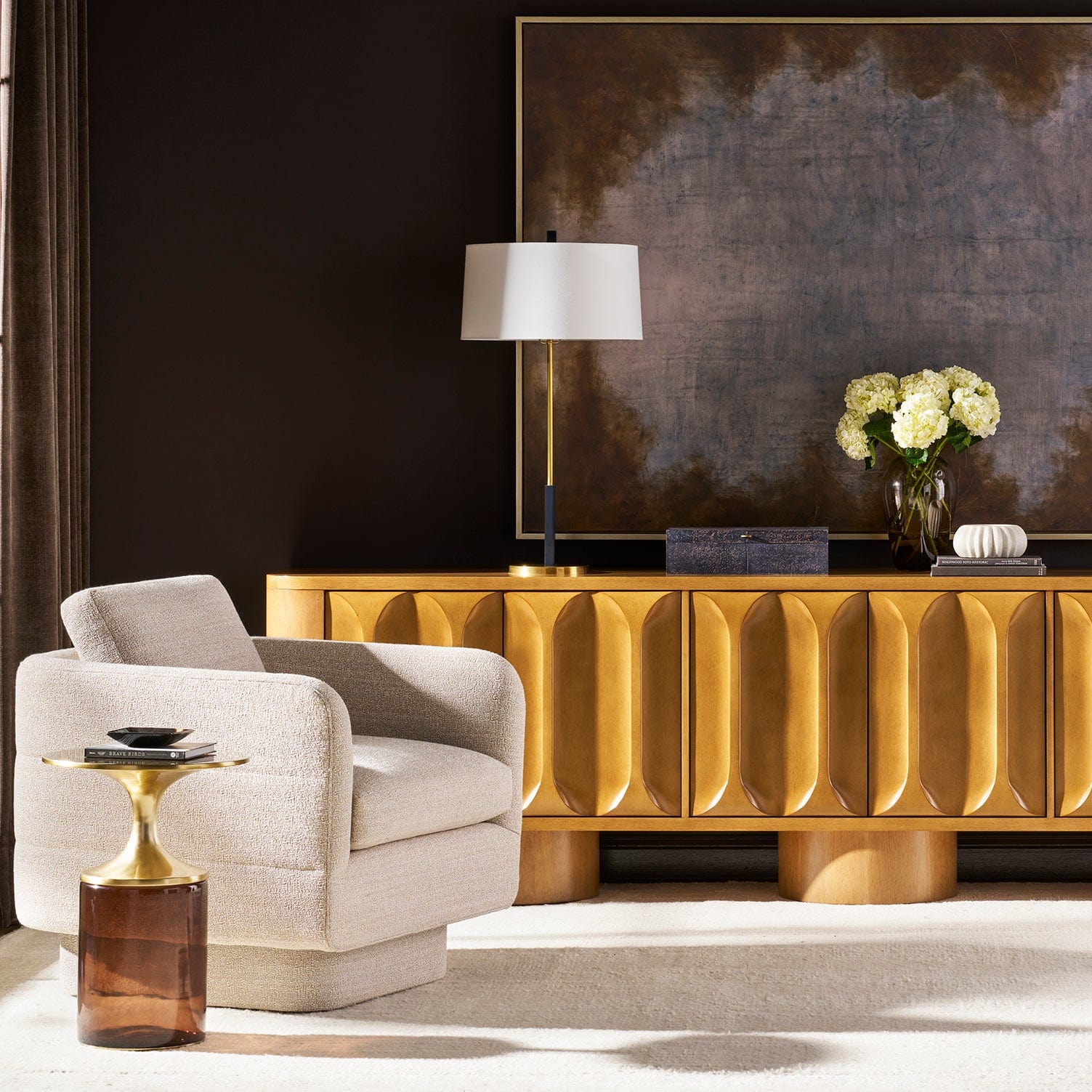 Modern living room with a gold sideboard, gray armchair, Aiden Spot table and decorative lamp.