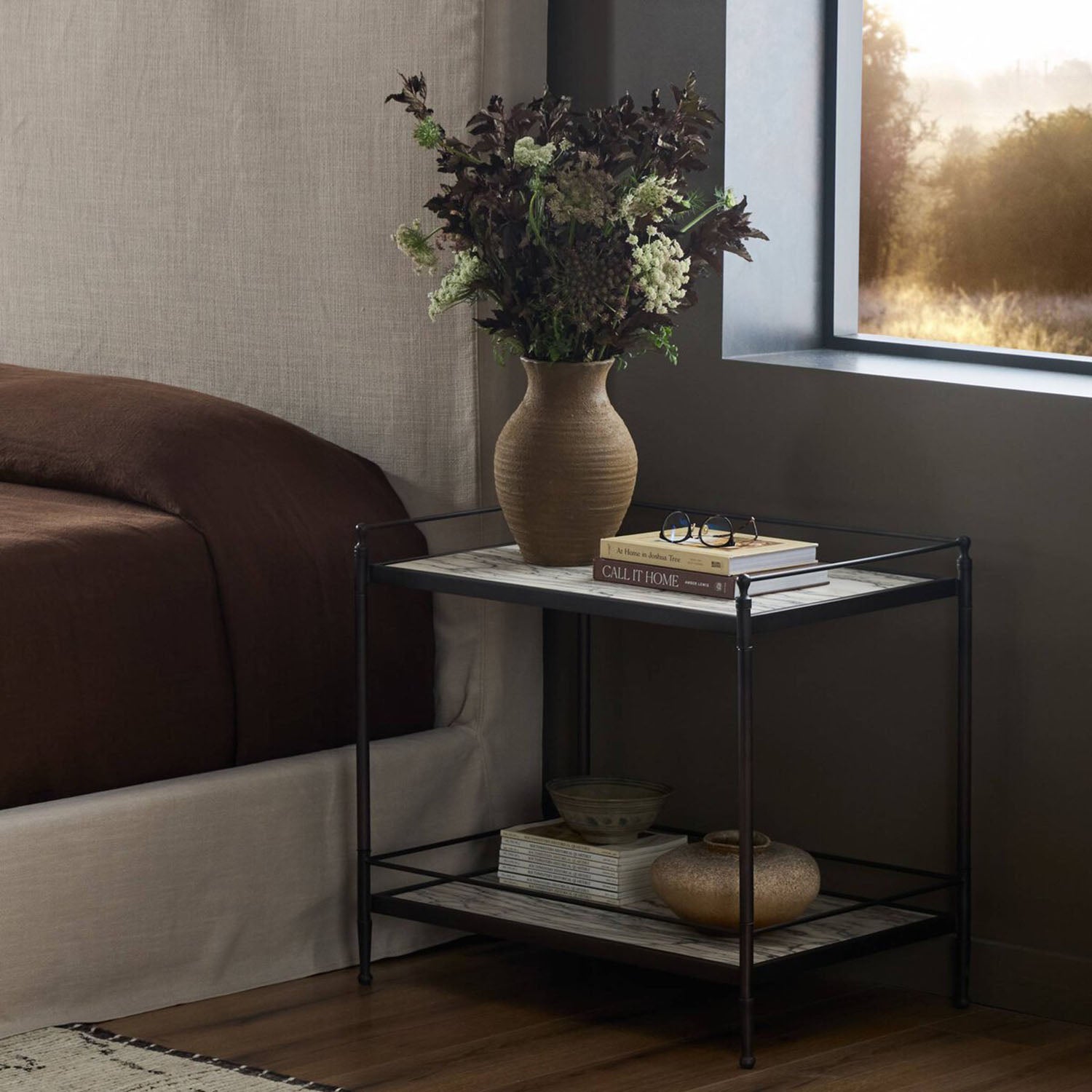 Eisen Two-tier nightstand with a vase of flowers and books in a bedroom setting.