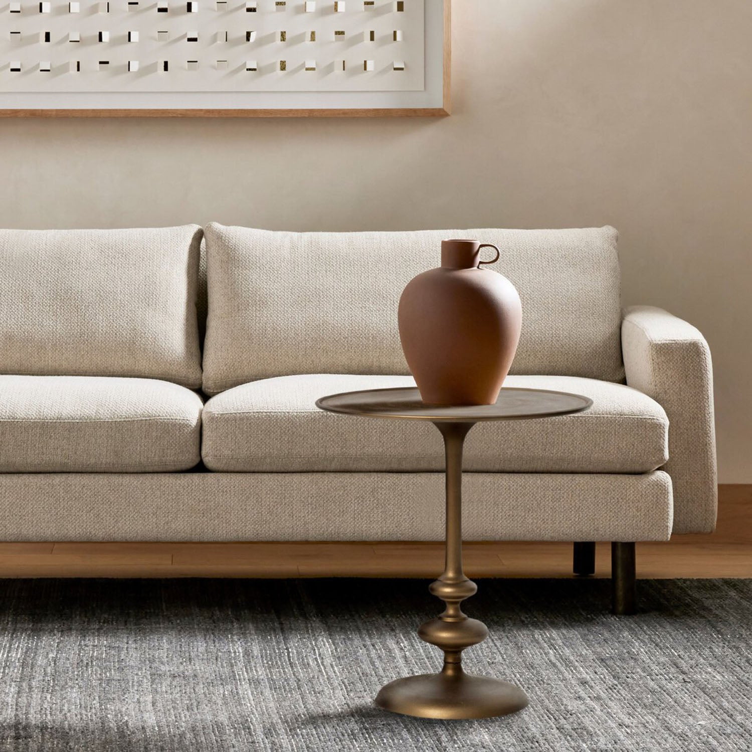Beige sofa with a brass Marlow round table and decorative vase in a living room setting.
