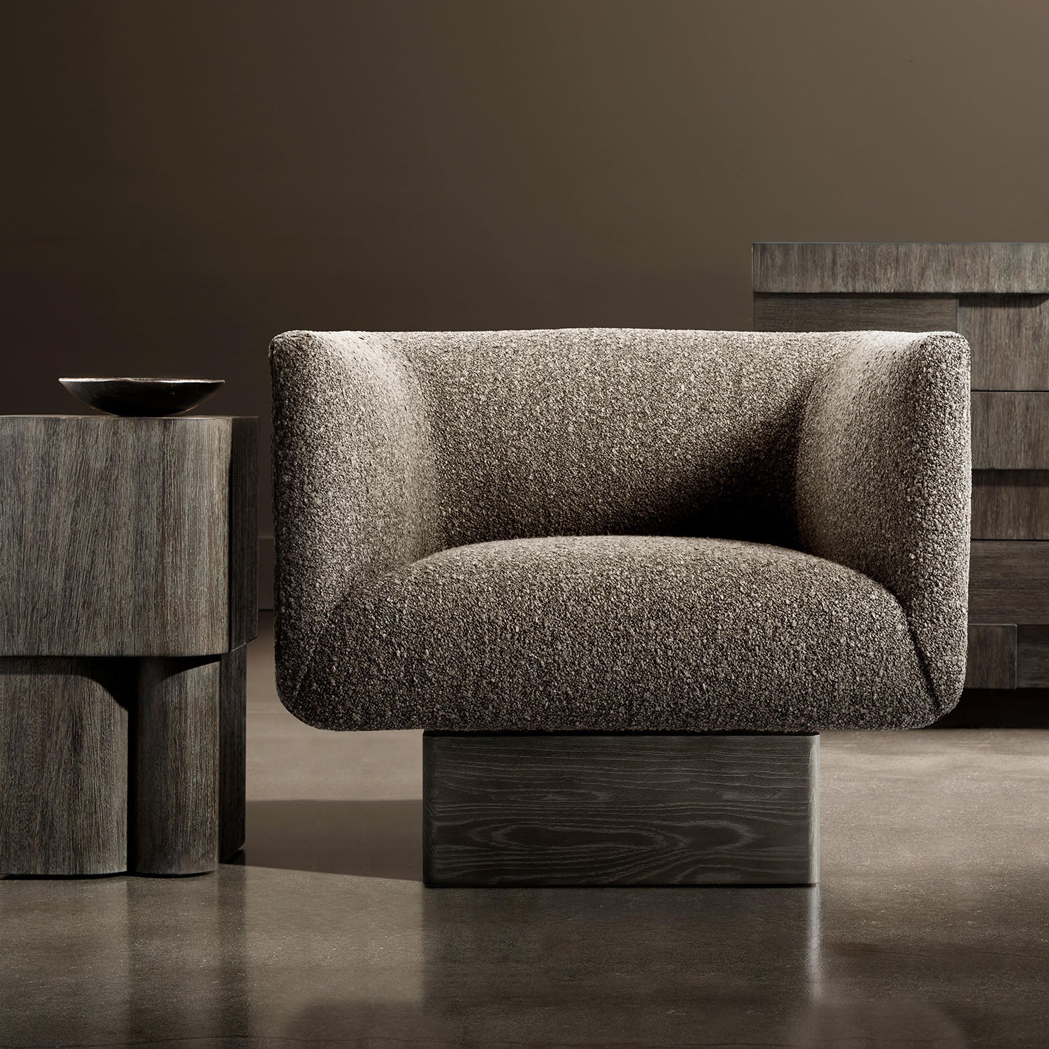 Modern Marni swivel armchair in a minimalistic setting with a dark brown wall and wooden table.