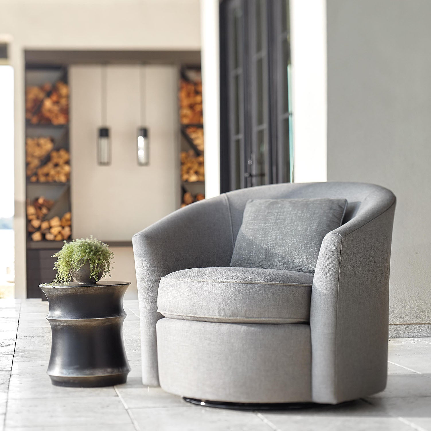 Gray swivel chair in a modern living room setting with a plant and Maya accent
table.