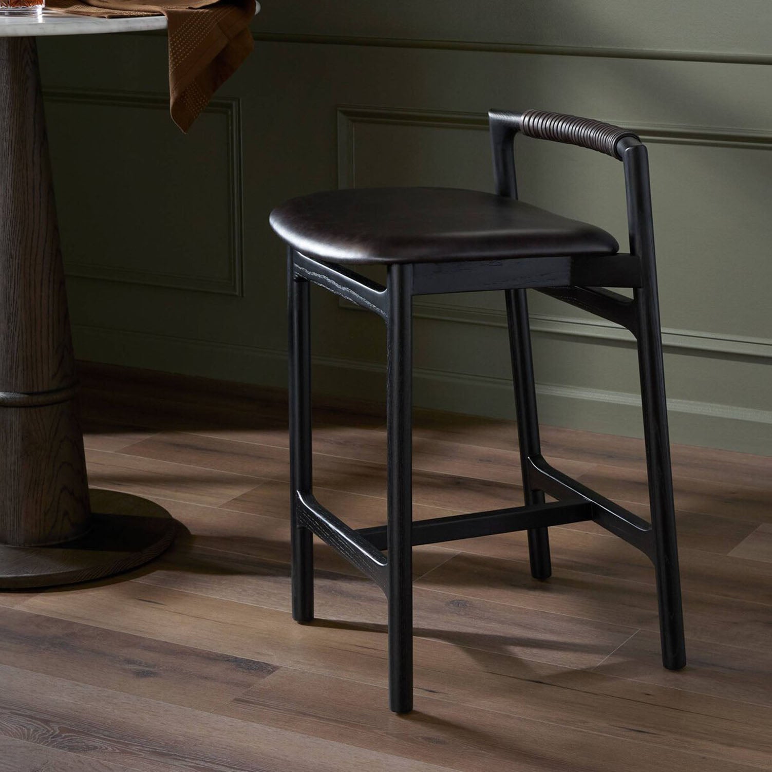 Baden Dark wooden bar stool with a cushioned seat in a room with green walls and wooden flooring.