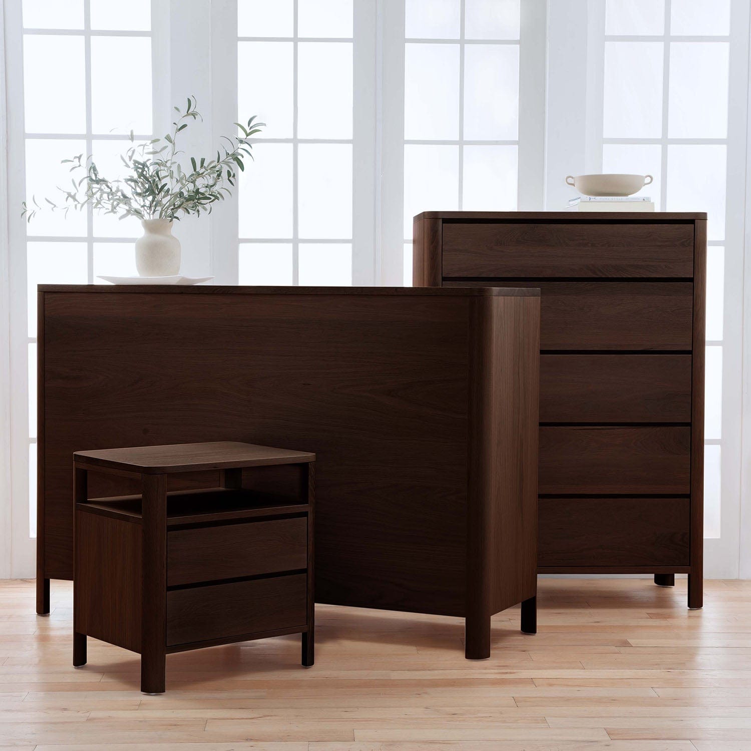 Set of dark wood furniture including a bed, nightstand, and dresser in a bright room.