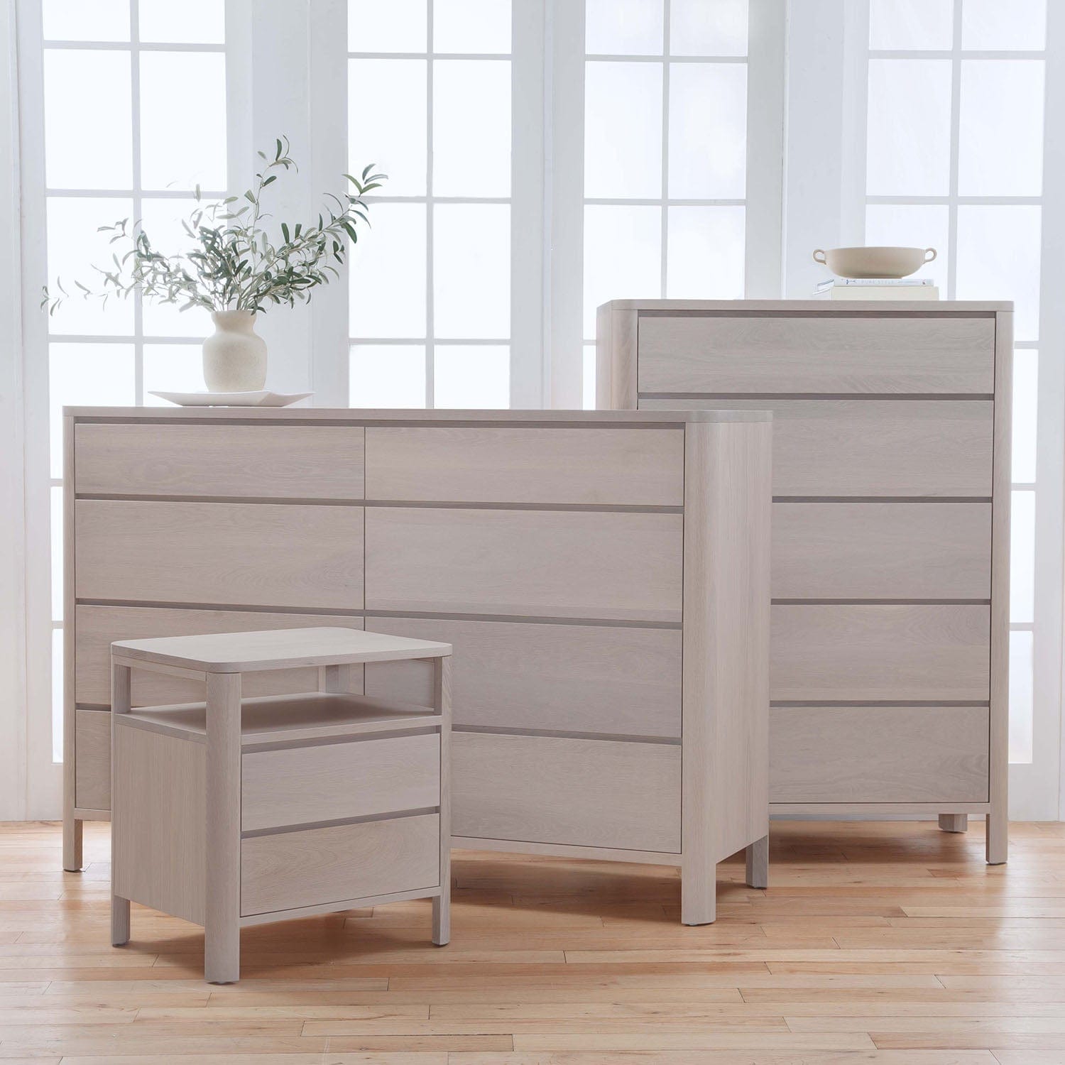Light wood dresser and nightstand set in a bright room with large windows.