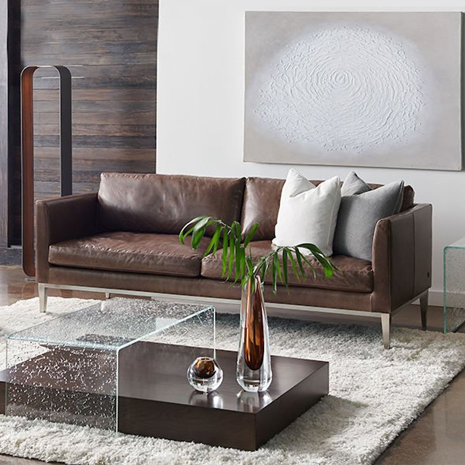 Modern living room with a brown leather Henley sofa, glass coffee table, and abstract art on the wall.