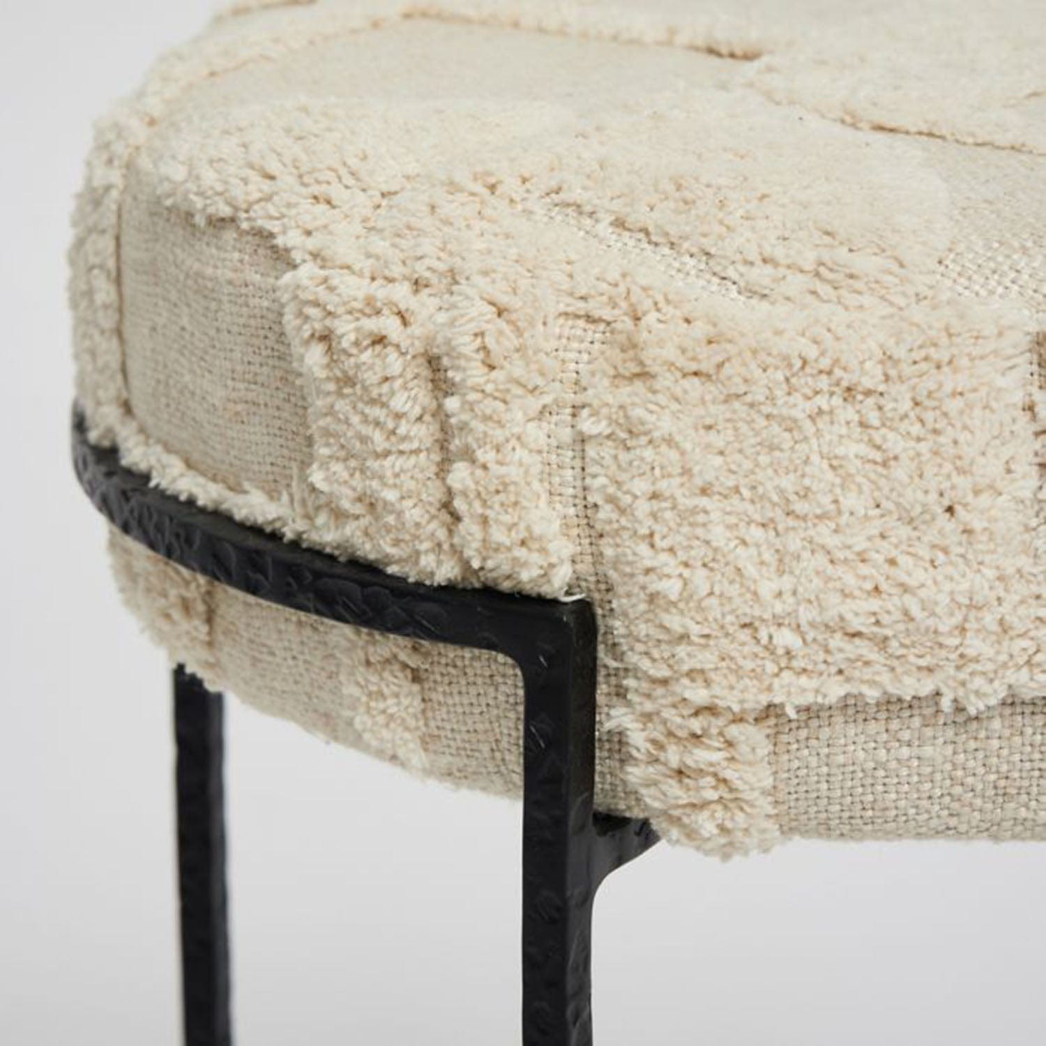 Round ottoman with textured beige cushion and black metal legs on a white background