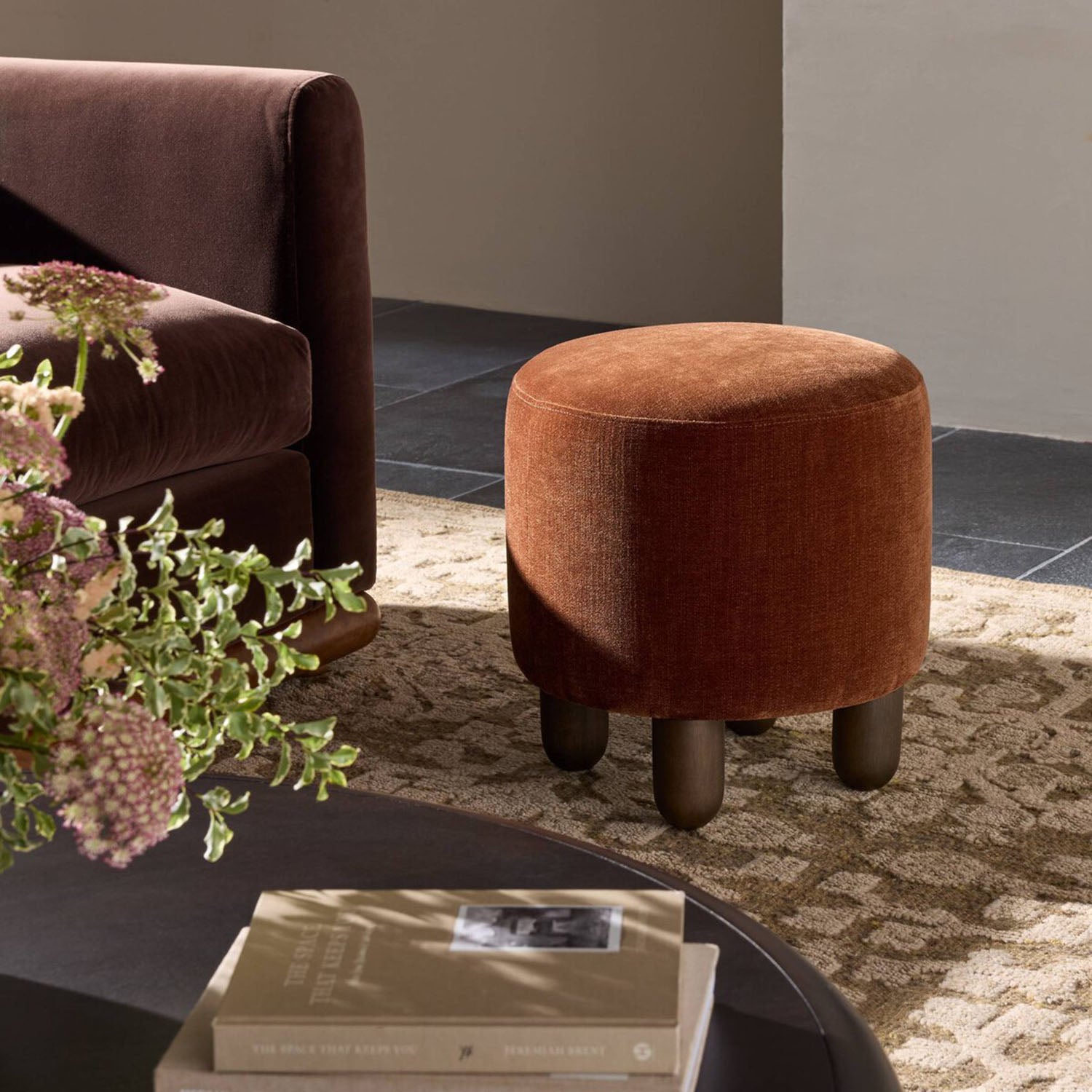 ZENA ottoman in a living room setting with a sofa, books, and a plant.