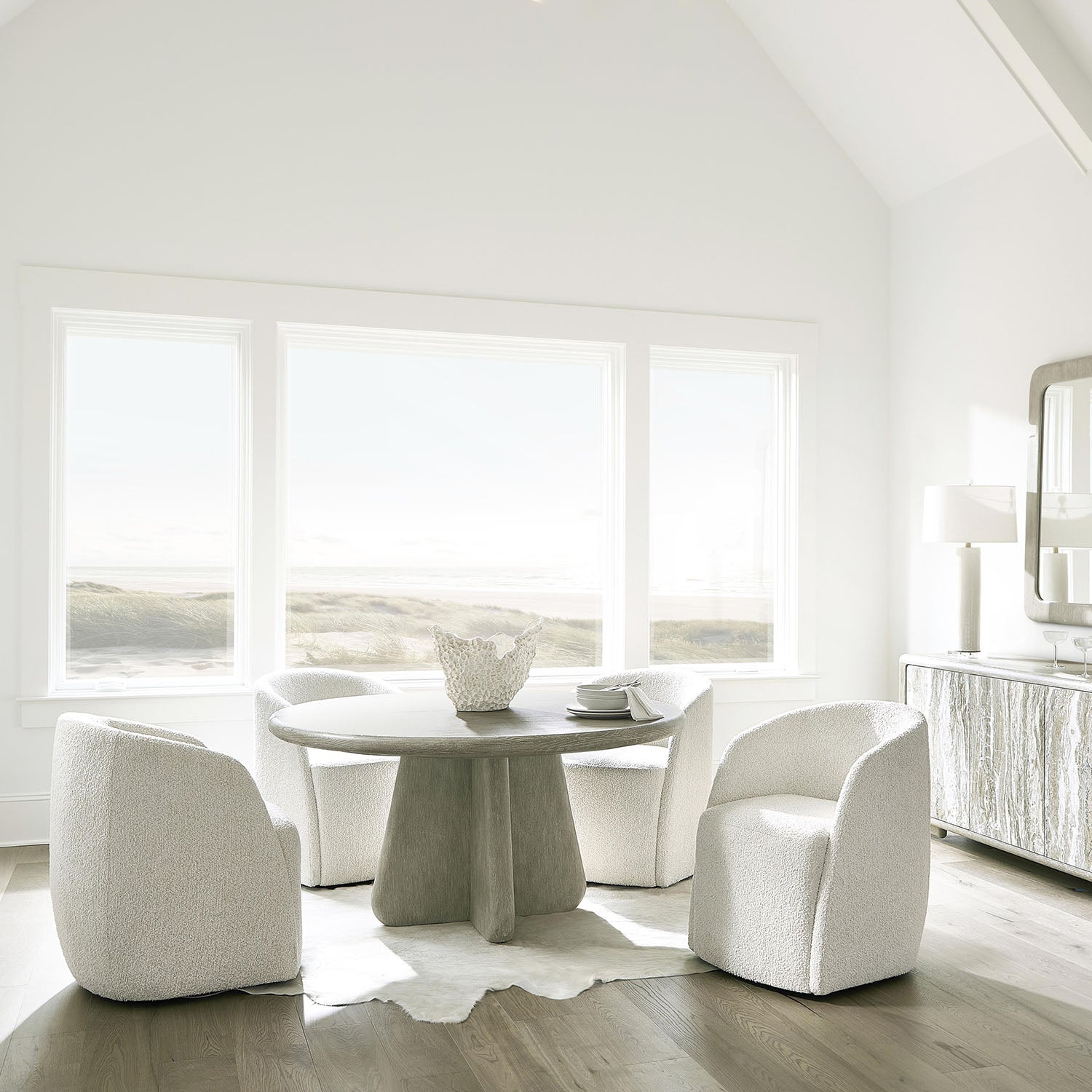Modern dining room with a round marble table and white Arcadia armchairs in a bright room.